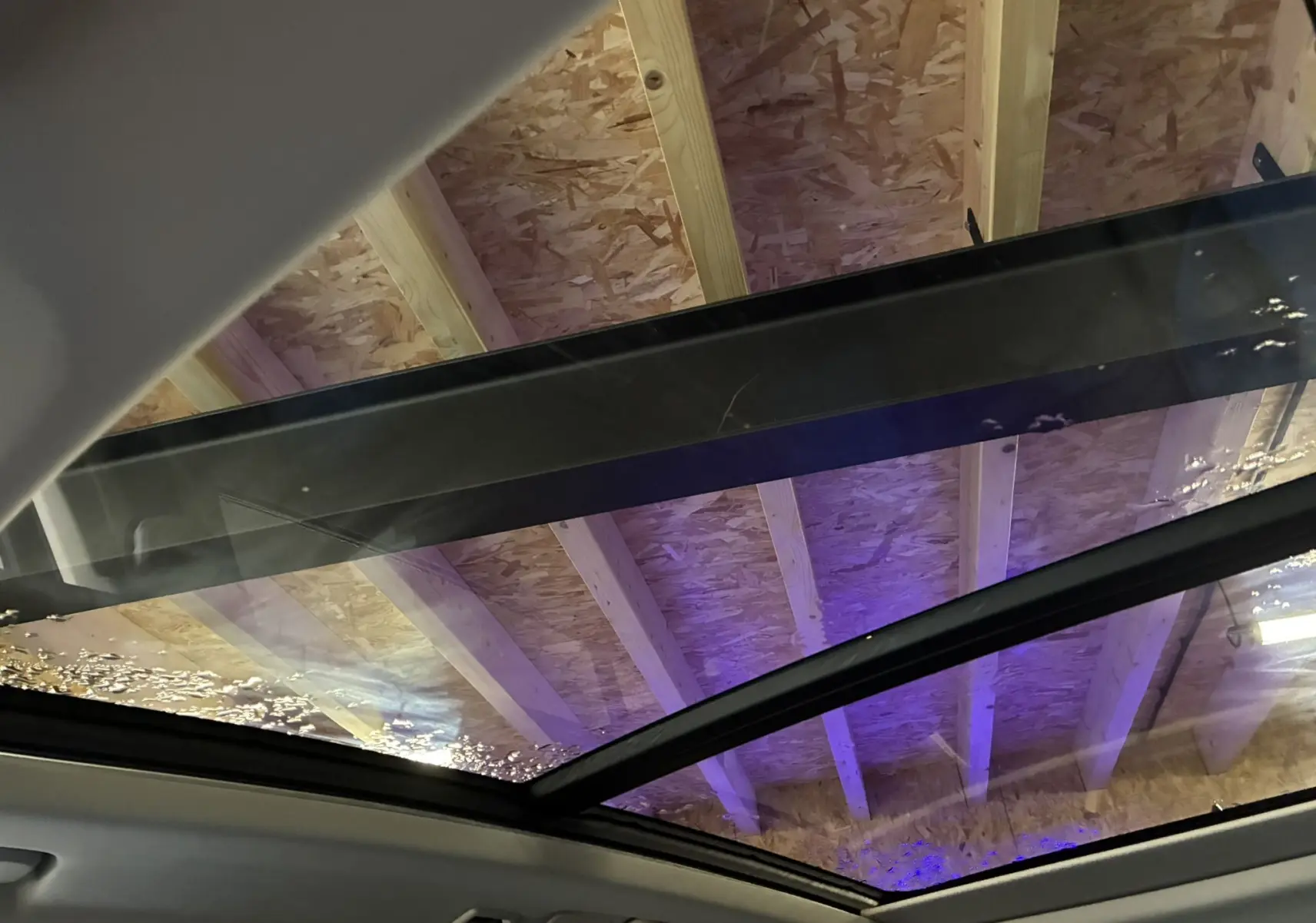 Toit panoramique en verre du LYNK & CO 01 bleu hybride rechargeable, vue intérieure vers le plafond en bois avec éclairage violet.