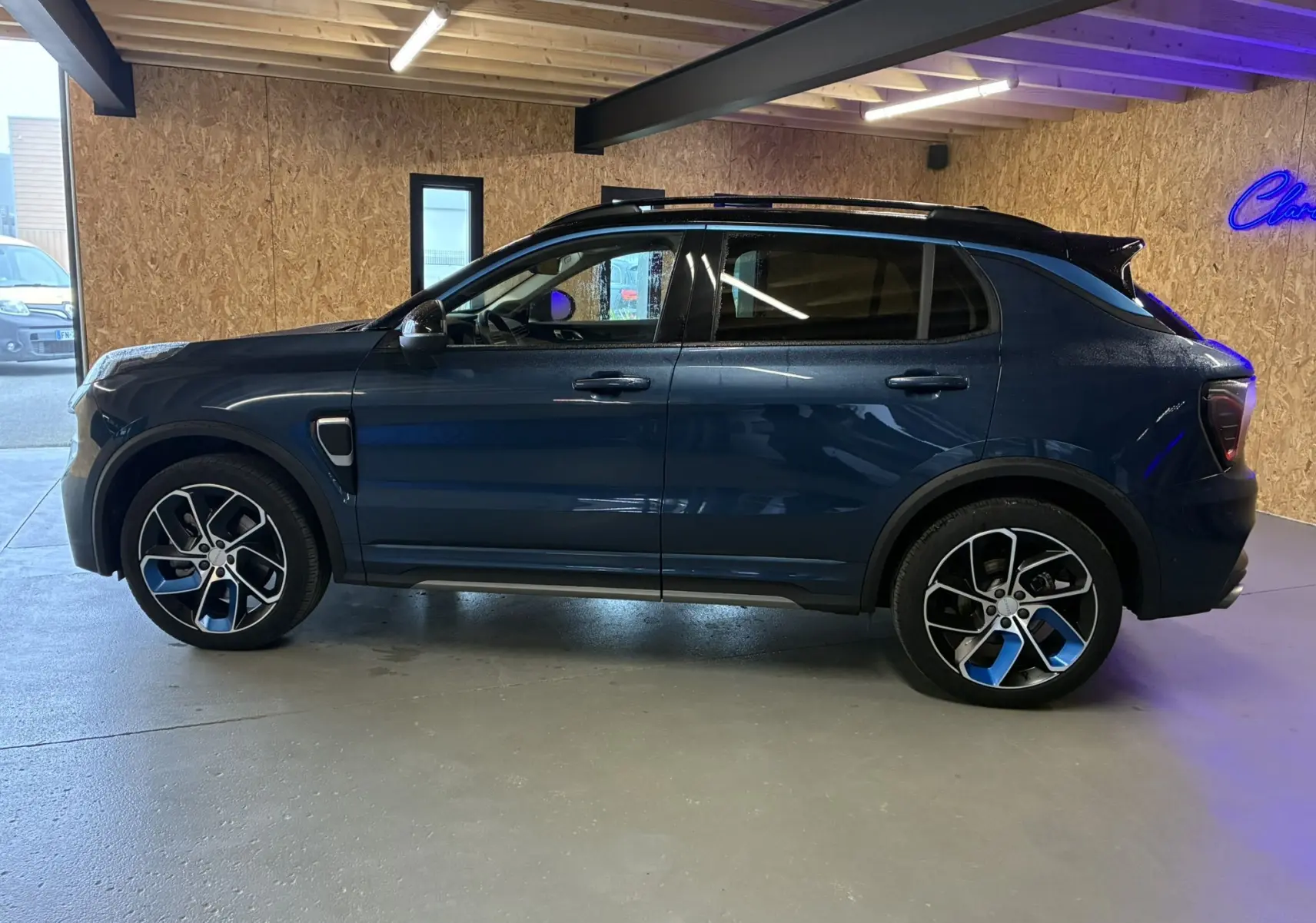 Profil côté gauche du SUV hybride rechargeable Lynk & Co 01 bleu 2023, avec jantes sport et toit noir en intérieur.