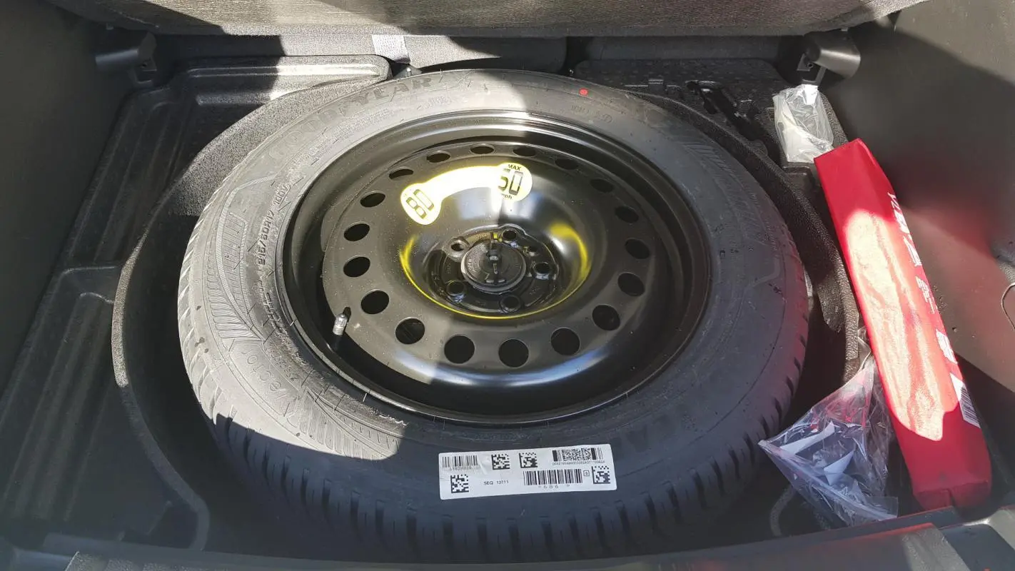 Vue plongeante sur la roue de secours noire dans le coffre du Jeep Compass blanc 2024, avec kit de secours rouge à côté.