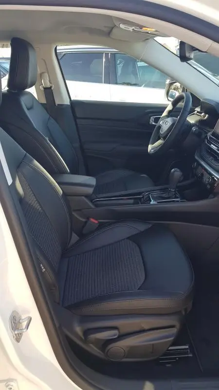 Vue intérieure côté conducteur du Jeep Compass blanc 2024, sièges noirs, accoudoir central et tableau de bord avec écran tactile.