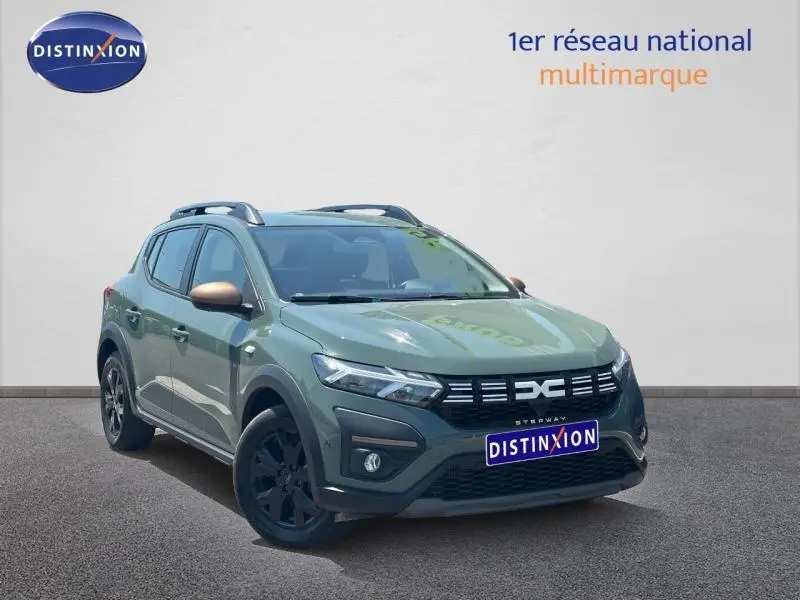 Vue 3/4 avant droite d'une Dacia Sandero Stepway 2025 vert cèdre métallisé avec jantes noires et barres de toit.