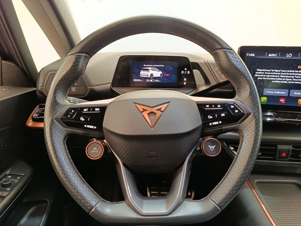 Vue rapprochée du volant cuir perforé gris foncé avec logo CUPRA orange et tableau de bord numérique du CUPRA BORN 2023.