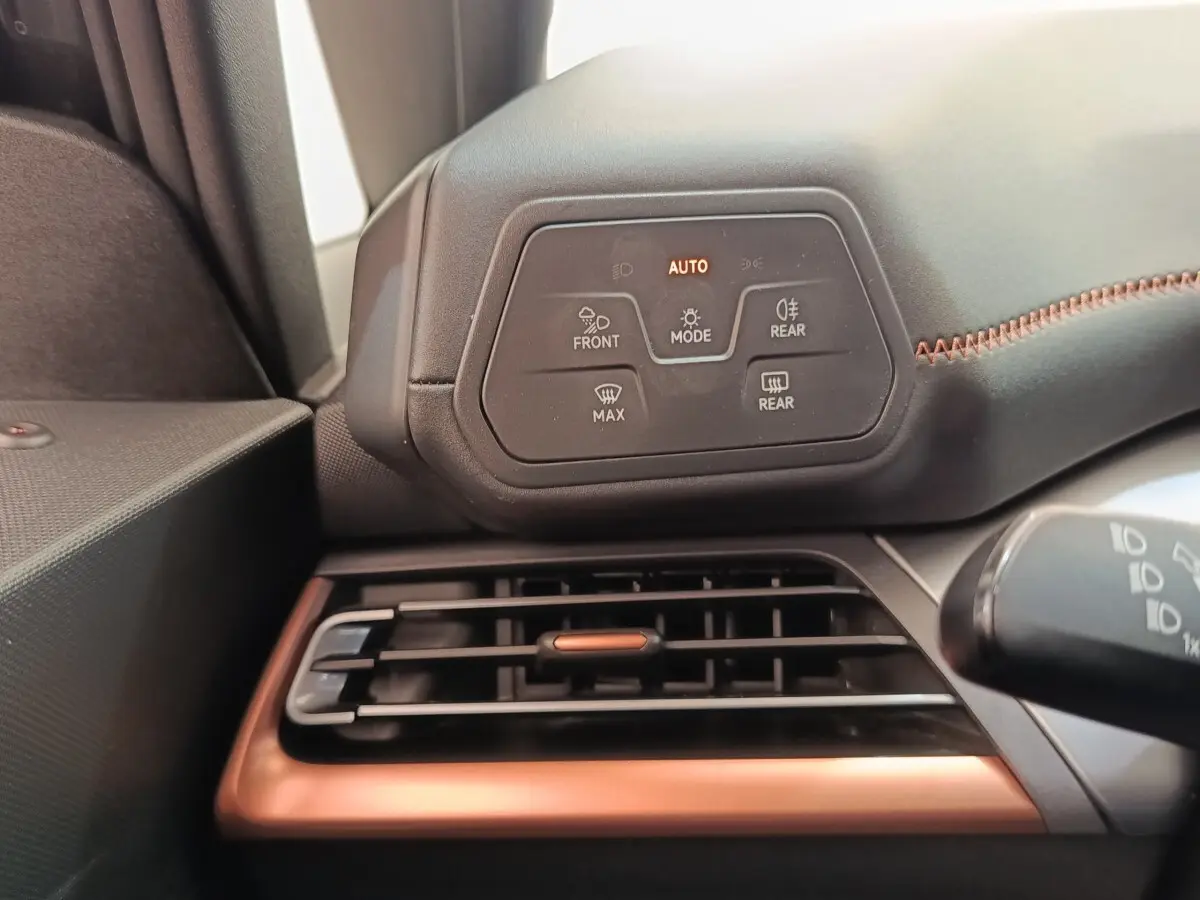 Détail du tableau de bord côté gauche avec commandes d’éclairage et grille d’aération cuivrée dans une CUPRA Born gris foncé.
