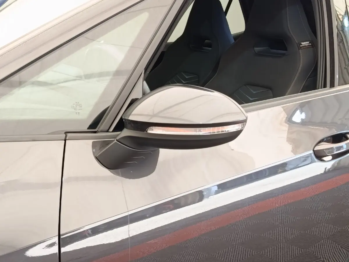 Gros plan sur le rétroviseur côté gauche gris foncé d’une CUPRA BORN 230ch avec siège sport visible à l’intérieur.