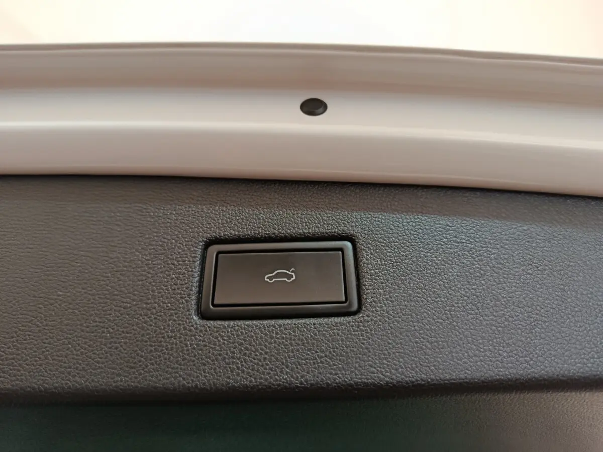 Bouton noir d'ouverture électrique du coffre sur la partie intérieure du hayon d'un Volkswagen Tiguan blanc.