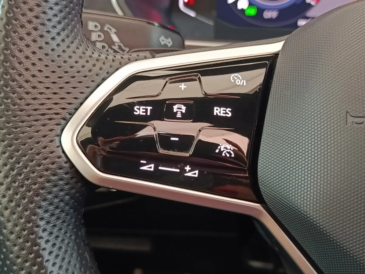 Gros plan sur les commandes du volant cuir perforé du Volkswagen Tiguan 1.4 eHybrid blanc, boutons de régulateur adaptatif.