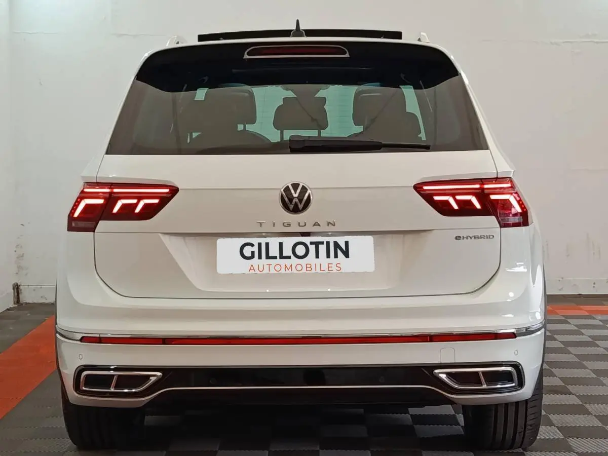 Vue arrière d'un Volkswagen Tiguan blanc hybride rechargeable avec feux LED allumés et double sortie d'échappement intégrée.