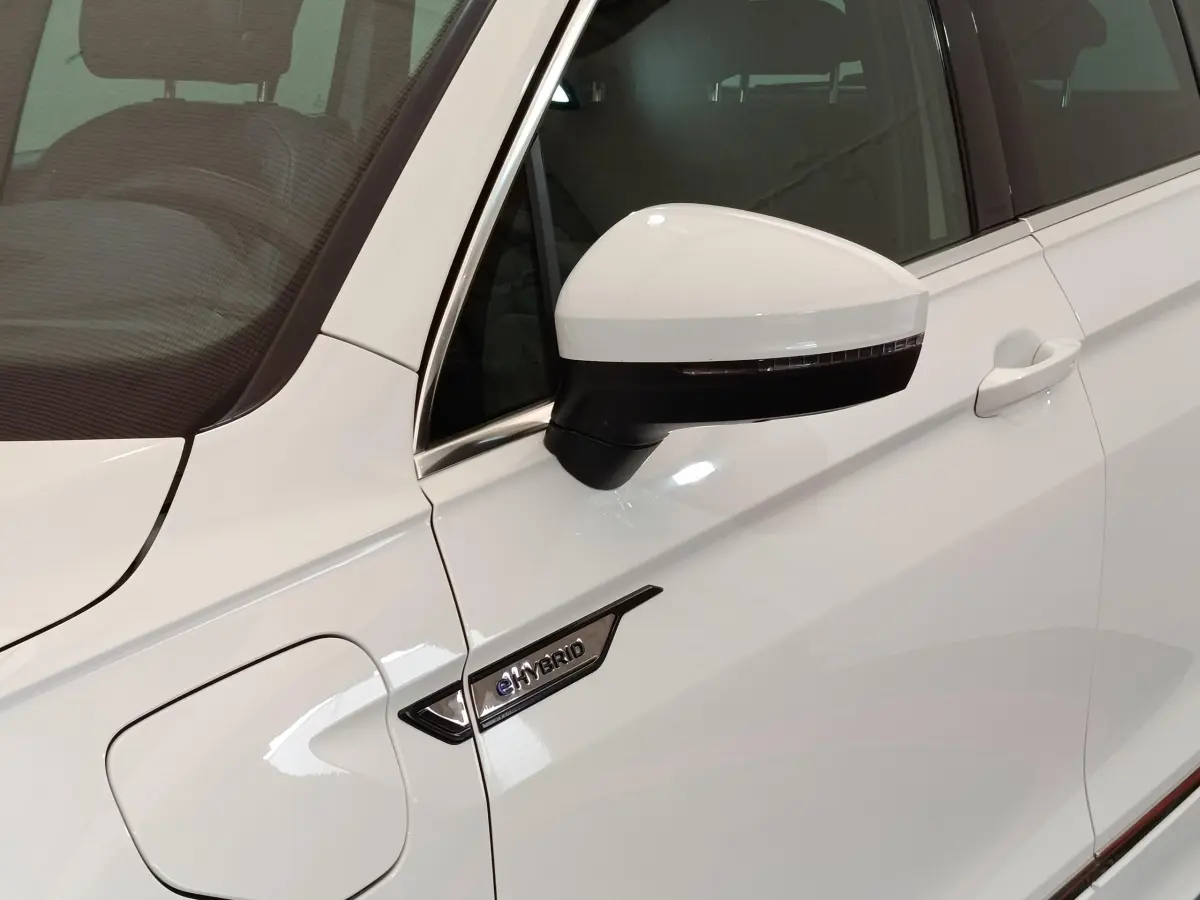 Gros plan sur la porte avant gauche blanche d’un Volkswagen Tiguan eHybrid avec rétroviseur et badge eHybrid visible.