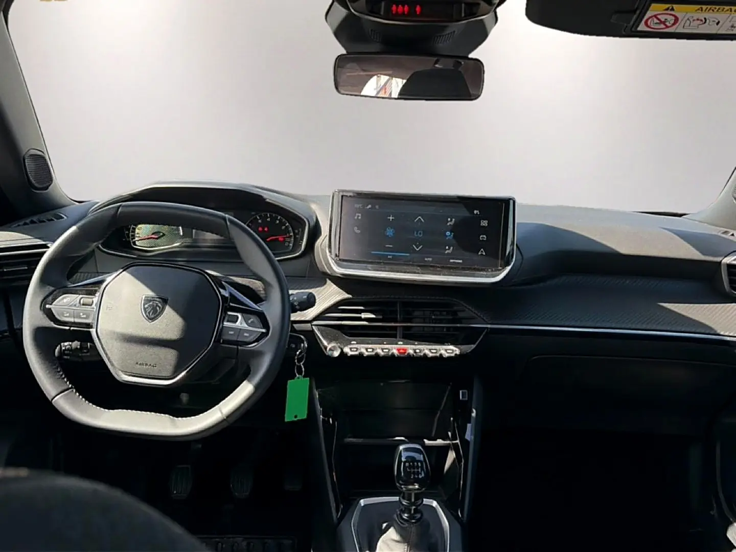Vue intérieure frontale du tableau de bord et volant du Peugeot 2008 gris, avec écran tactile et levier de vitesse manuel.