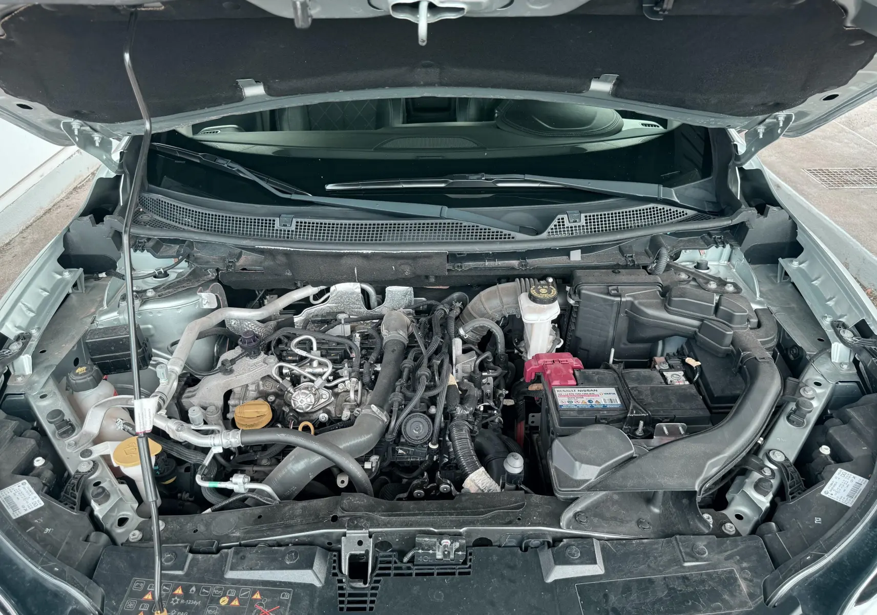 Moteur essence du Renault Kadjar gris vu de dessus avec capot ouvert, montrant les composants mécaniques et la batterie.