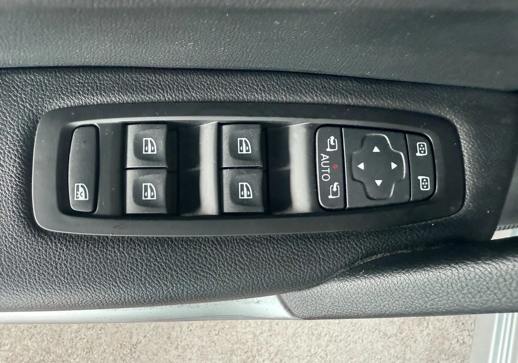 Gros plan sur les commandes de lève-vitres et réglages des rétroviseurs côté conducteur d'un Renault Kadjar gris.