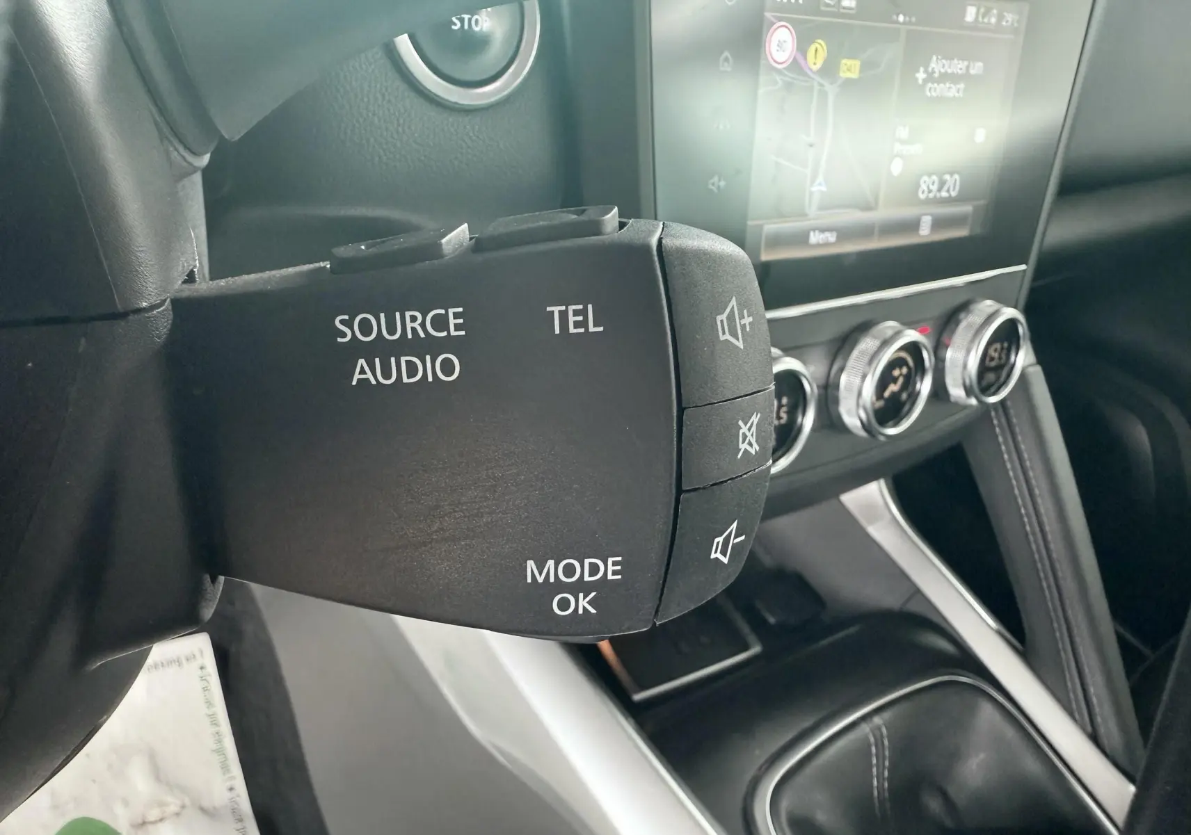 Gros plan sur la commande audio au volant du Renault Kadjar gris, avec tableau de bord et écran tactile en arrière-plan.