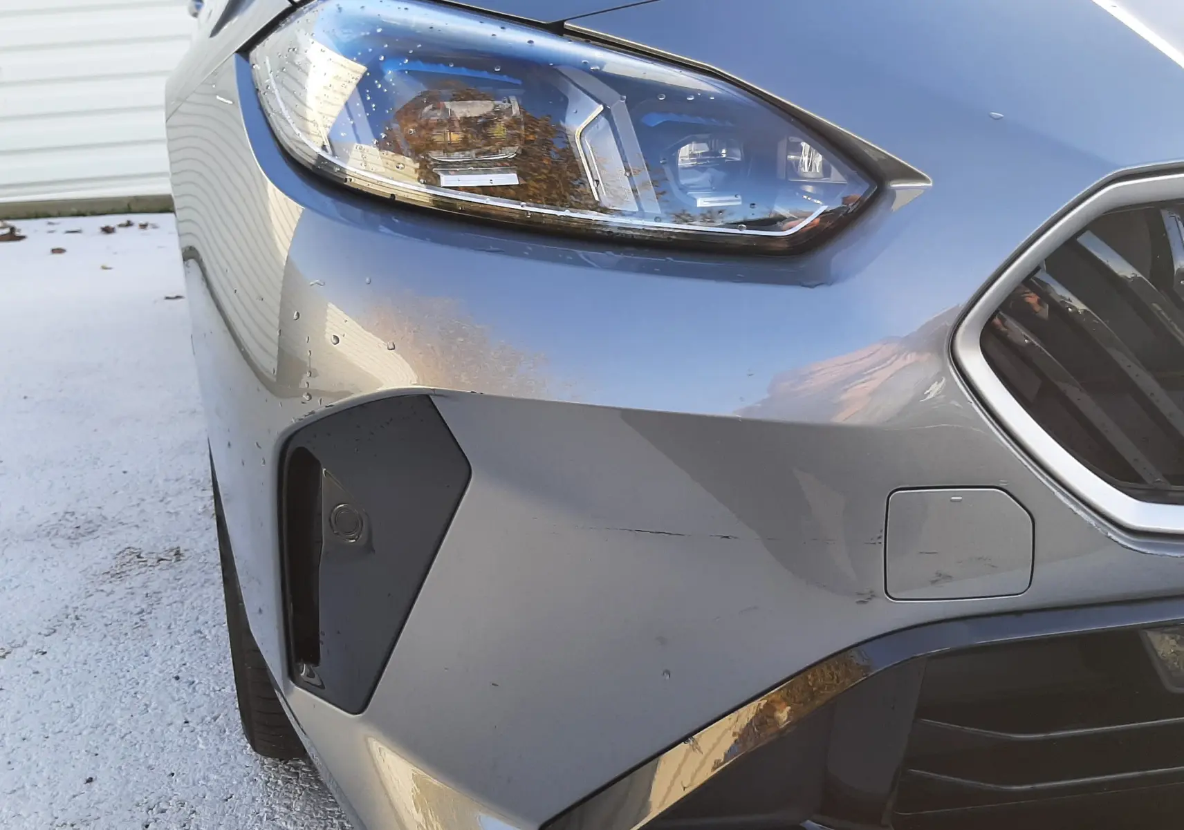 Gros plan sur l'avant droit d'une BMW Série 1 gris Skyscraper, mettant en valeur le phare LED et la calandre hexagonale.