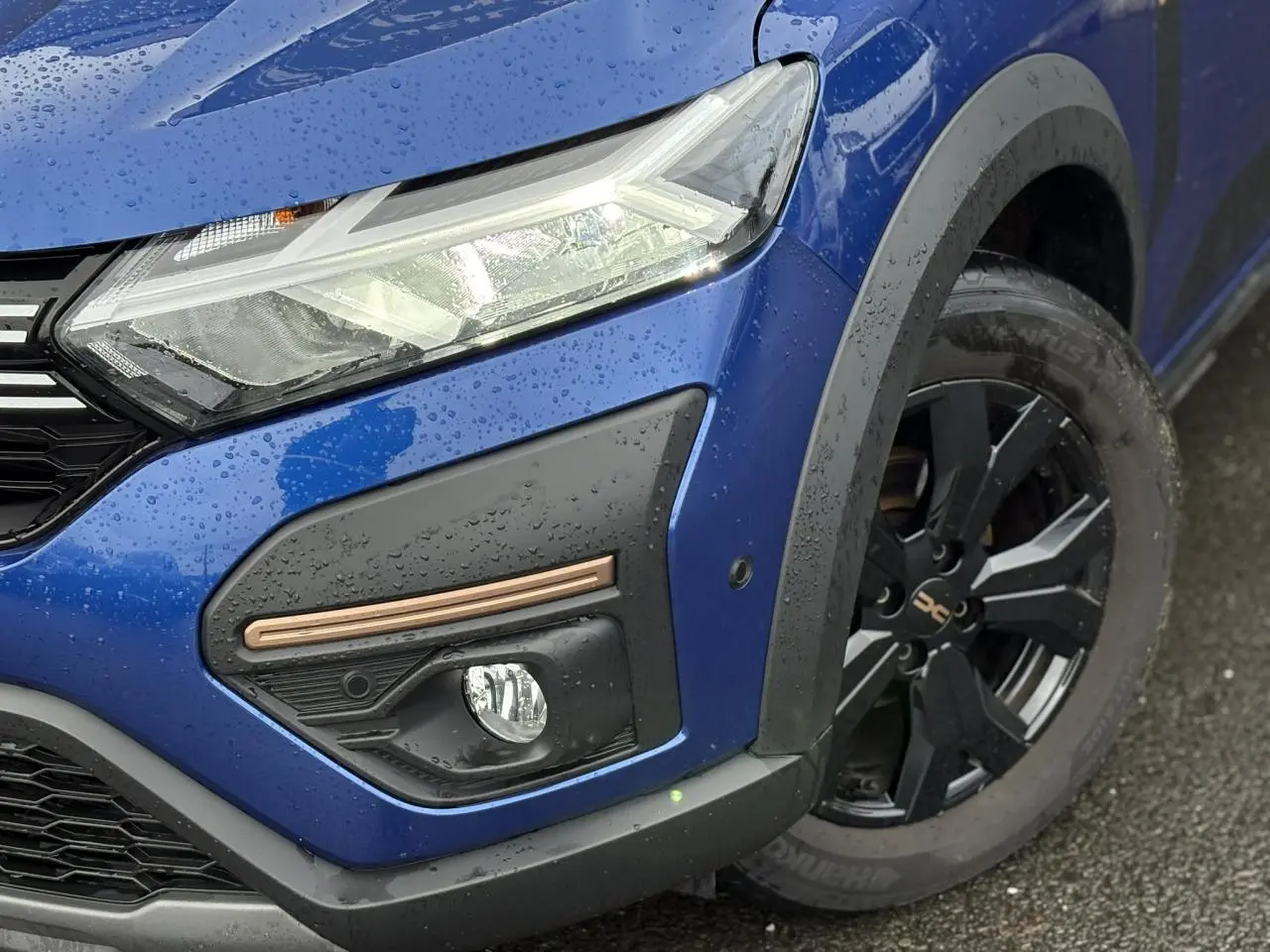 Gros plan sur l'avant droit bleu Iron du Dacia Sandero Stepway avec phare LED et jante alu noire.
