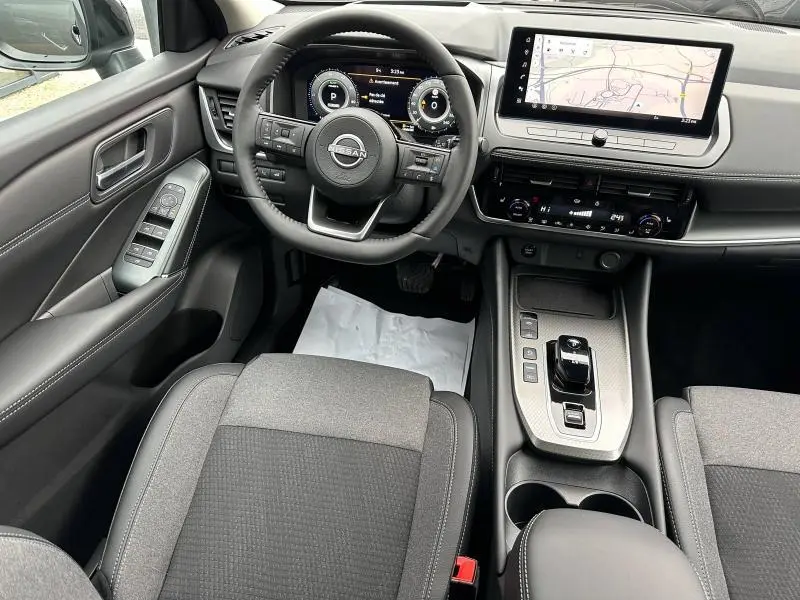 Vue intérieure avant du Nissan Qashqai Hybrid e-POWER 2025, tableau de bord moderne avec écran tactile et volant multifonction.