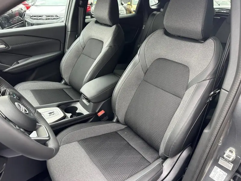 Vue intérieure côté conducteur du Nissan Qashqai Hybrid e-POWER 2025, sièges tissu gris et console centrale avec accoudoir.