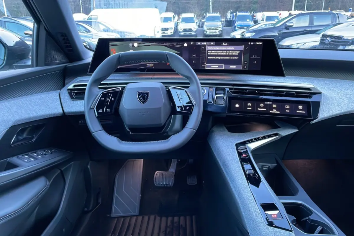 Vue intérieure du poste de conduite du Peugeot 5008 Hybrid 145 Allure Plus 2025, avec volant cuir multifonctions et écran panoramique incurvé.