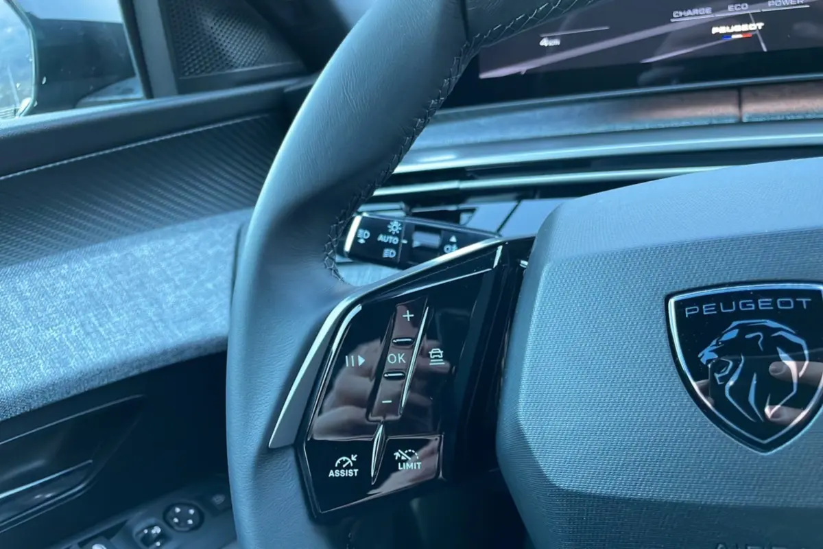 Gros plan sur le volant cuir multifonctions gris titane du Peugeot 5008 Hybrid 145, avec commandes intégrées et logo Peugeot.