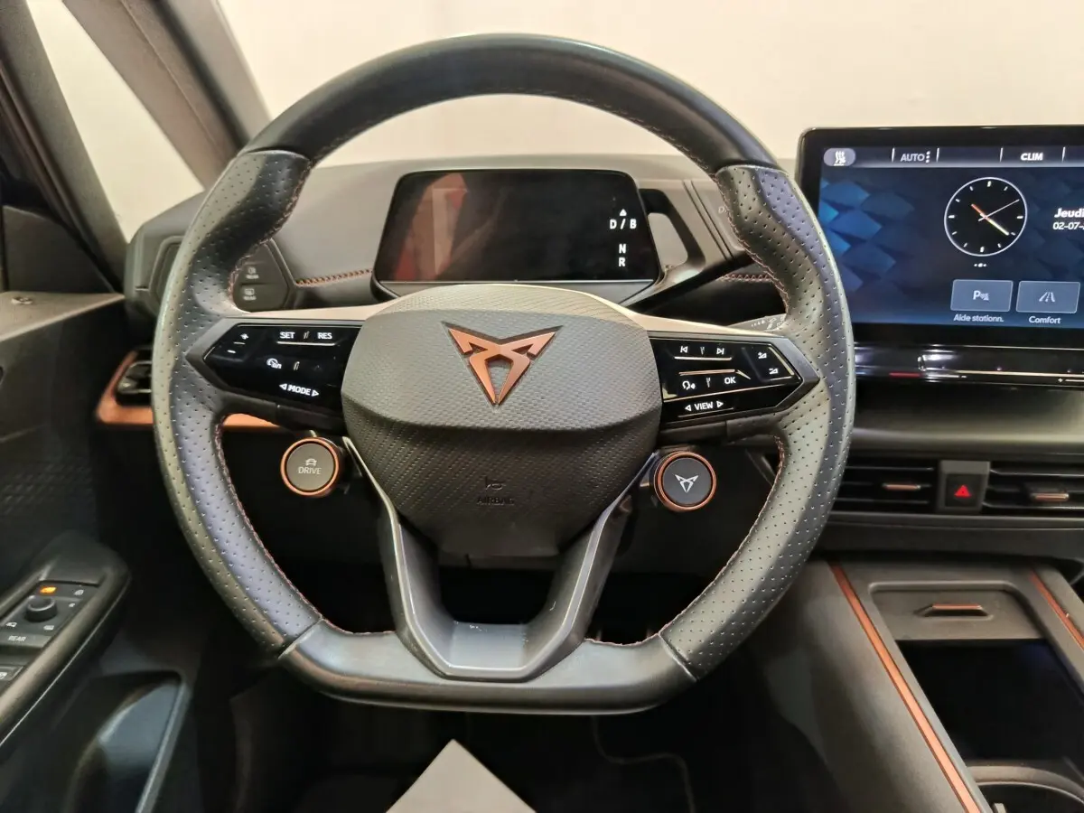 Vue intérieure centrée sur le volant noir perforé avec logo CUPRA cuivré et écran tactile du tableau de bord.