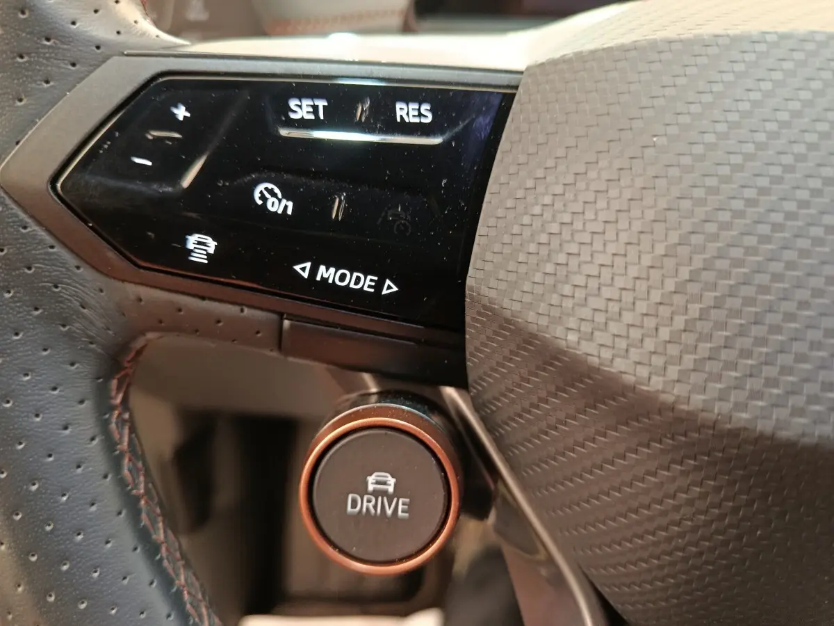 Gros plan sur les commandes du volant en cuir perforé du CUPRA BORN 230ch, bouton Drive et régulateur adaptatif visibles.