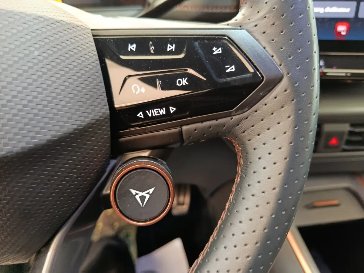 Gros plan sur le volant cuir perforé avec commandes tactiles et logo CUPRA sur molette en aluminium cuivré.