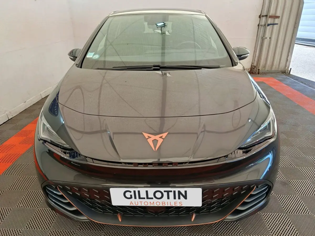 Vue avant plongeante d'une CUPRA BORN gris foncé avec logo cuivré et calandre noire ajourée dans un garage.