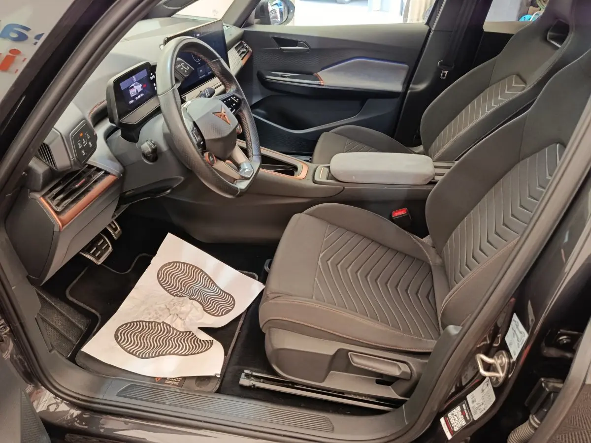 Intérieur avant droit du CUPRA BORN gris foncé 2023, sièges tissu avec surpiqûres orange et volant multifonctions cuir.