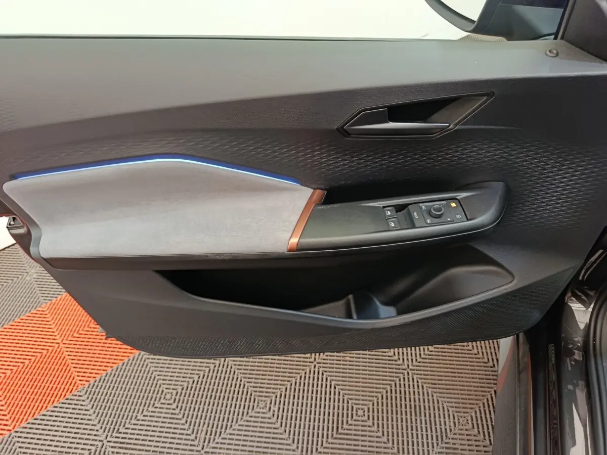 Vue rapprochée de la porte avant gauche du CUPRA Born gris foncé, avec habillage tissu clair et éclairage d'ambiance bleu.