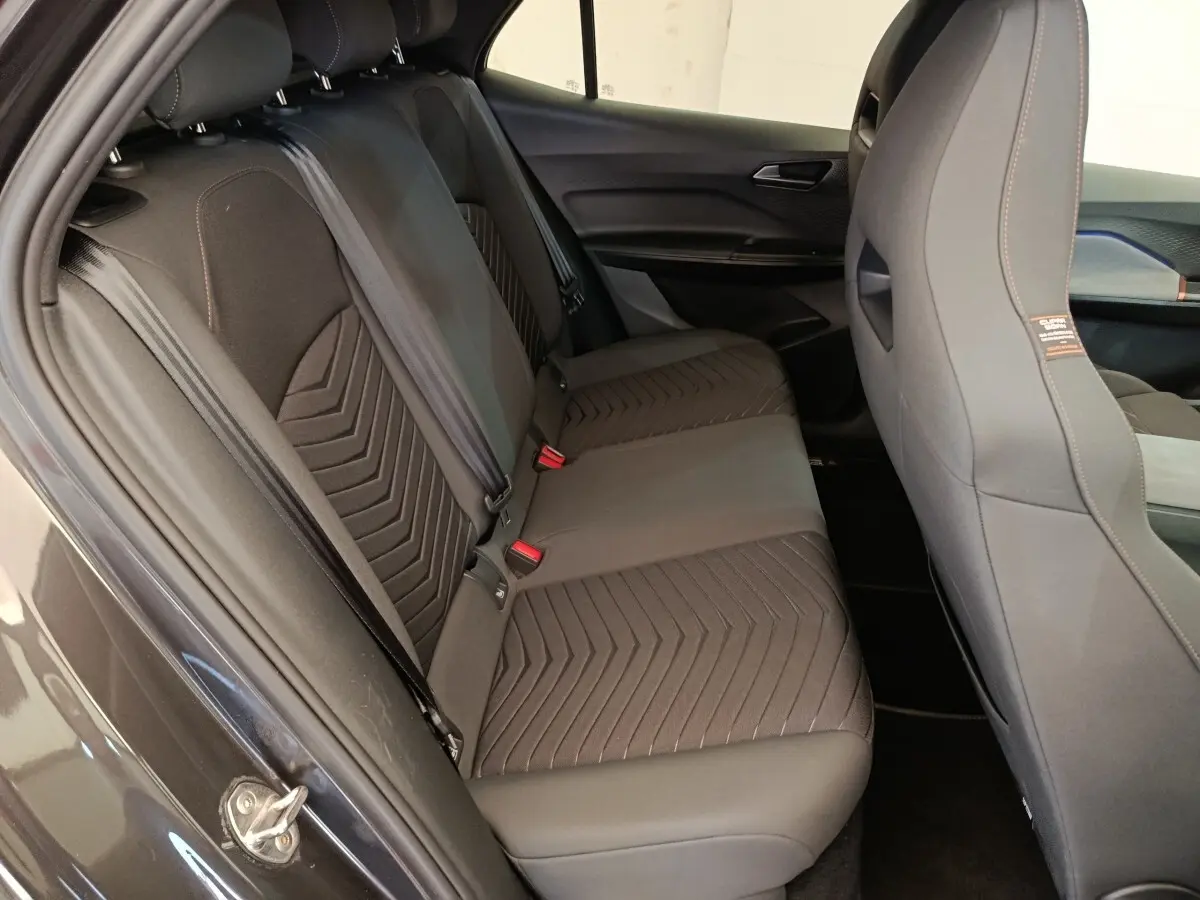 Vue intérieure côté gauche sur la banquette arrière grise foncée du CUPRA BORN 230ch avec sièges en tissu et ceintures visibles.