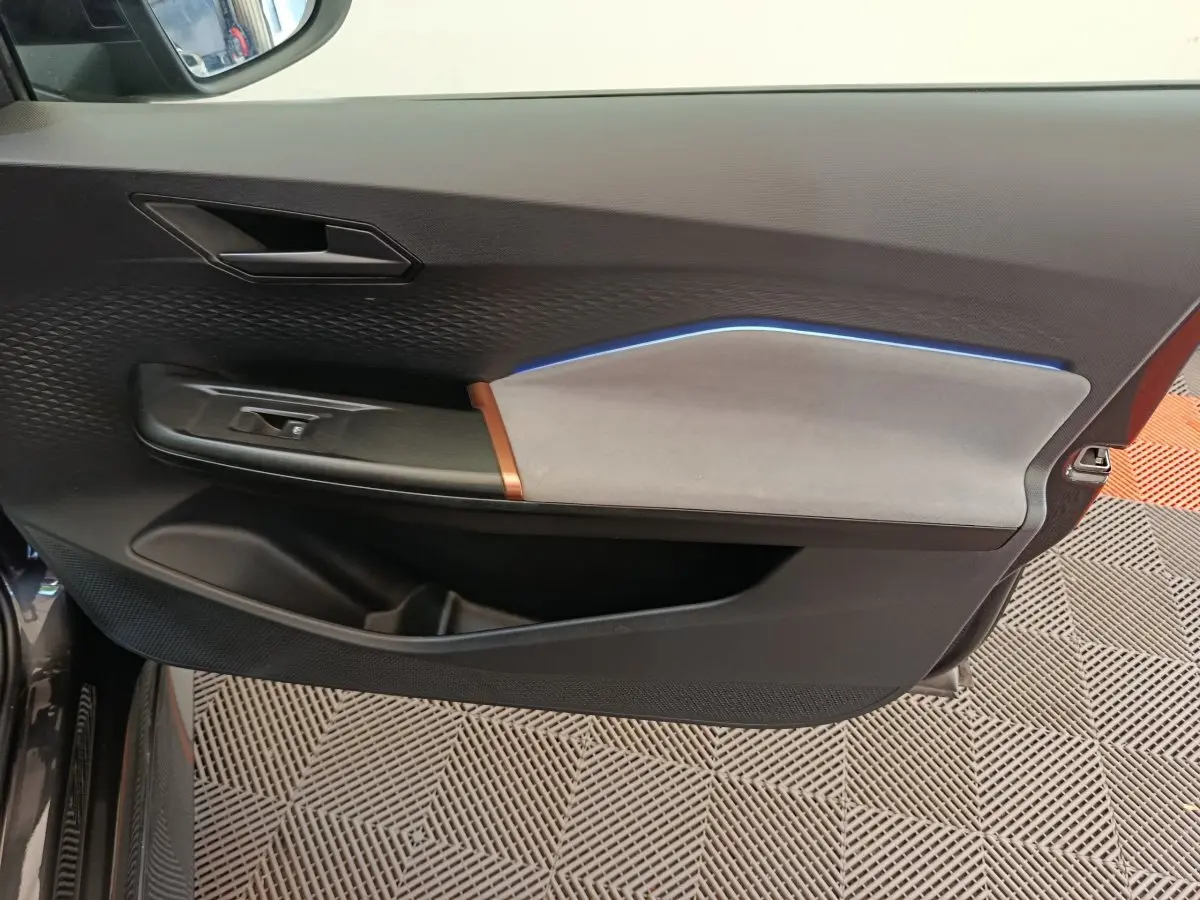 Vue intérieure côté gauche de la porte d’une CUPRA BORN gris foncé, avec éclairage d’ambiance bleu et garniture bicolore.