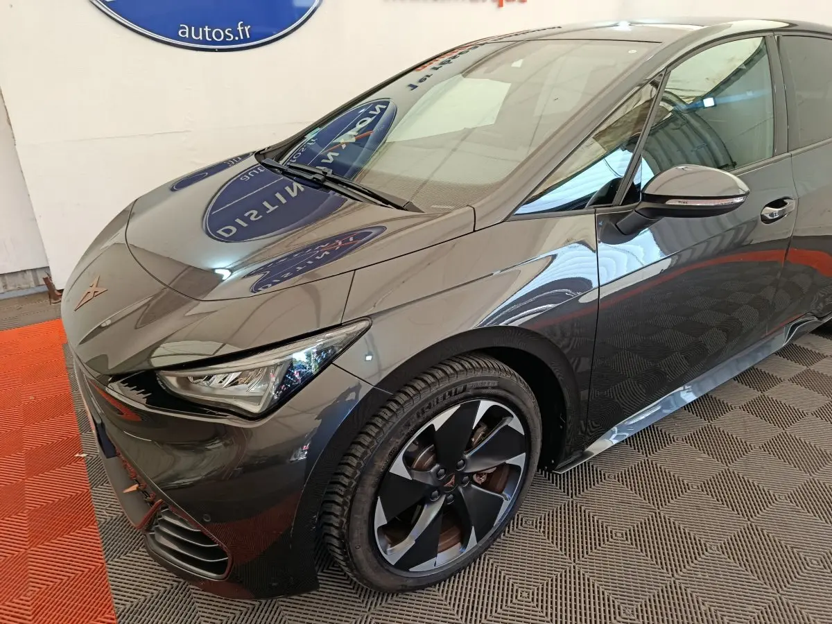 Vue 3/4 avant droit d'une CUPRA BORN gris foncé électrique avec jantes noires et détails orange sur le bouclier avant.