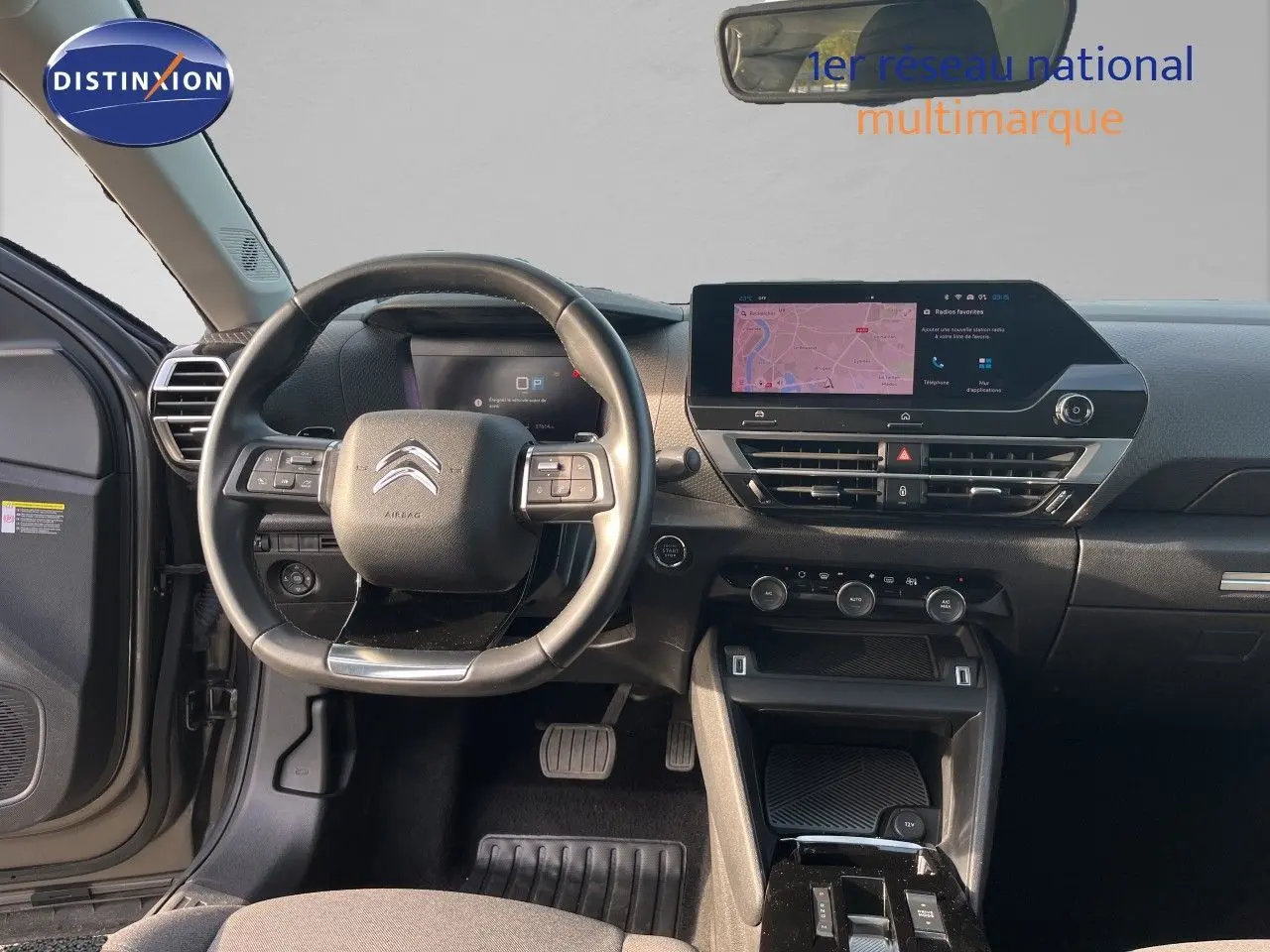 Vue intérieure avant centrée sur le volant et le tableau de bord noir du Citroën C4 gris 2023 avec écran tactile et commandes intégrées.