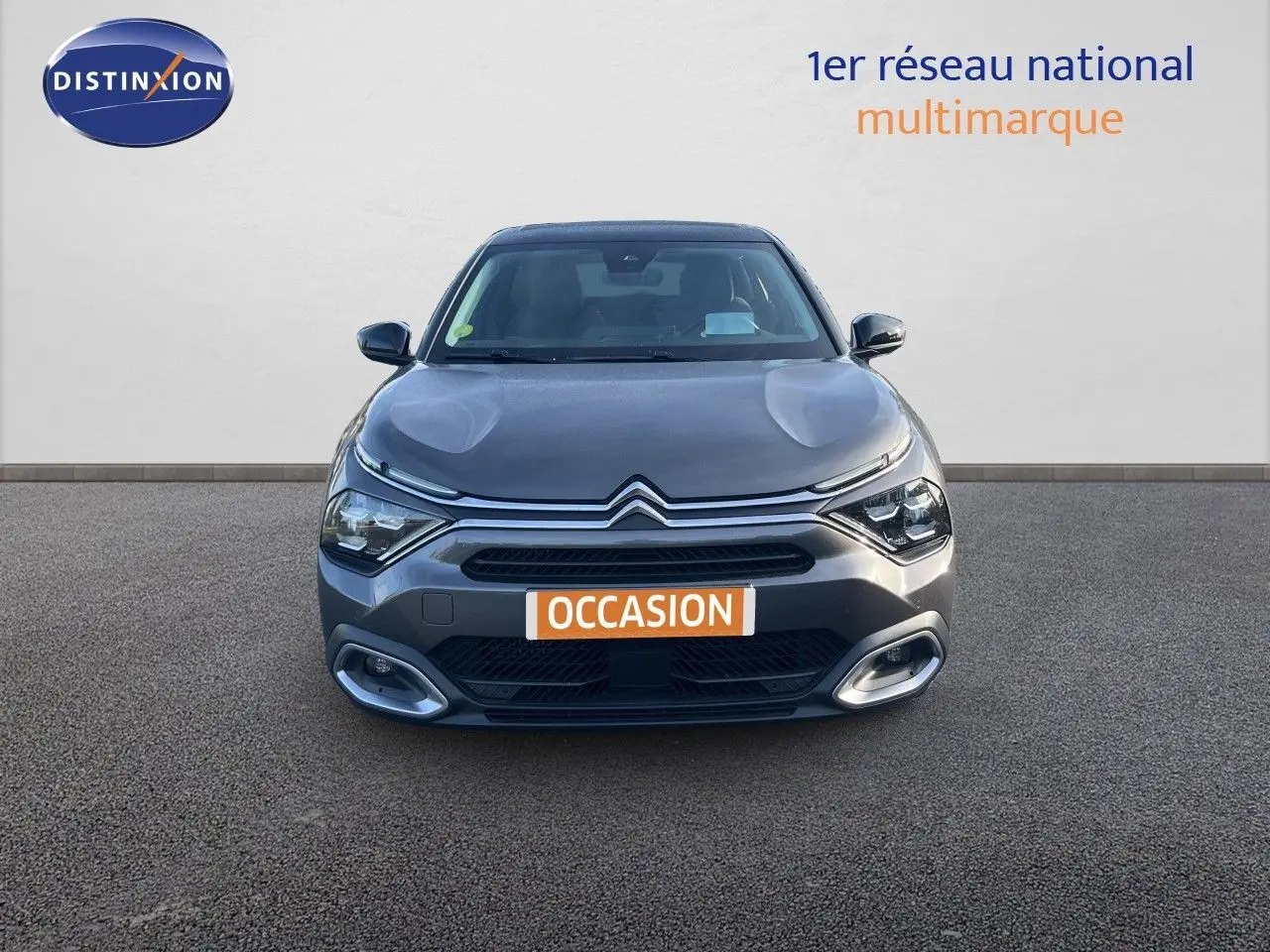 Vue frontale d'une Citroën C4 gris métallisé 2023 avec calandre distinctive et feux LED allumés.