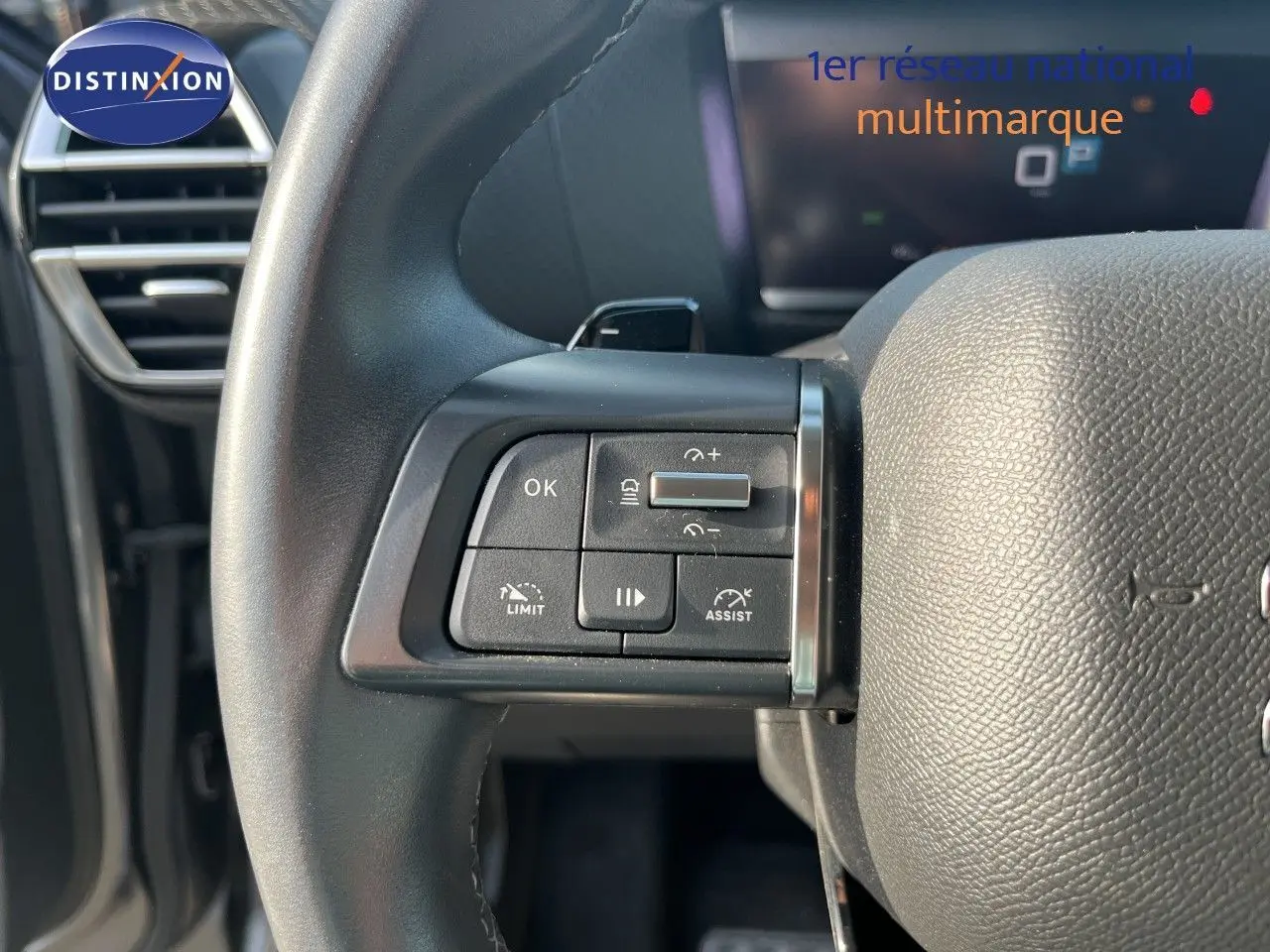 Gros plan sur les commandes à gauche du volant noir d'une Citroën C4 gris 2023, avec tableau de bord numérique en arrière-plan.