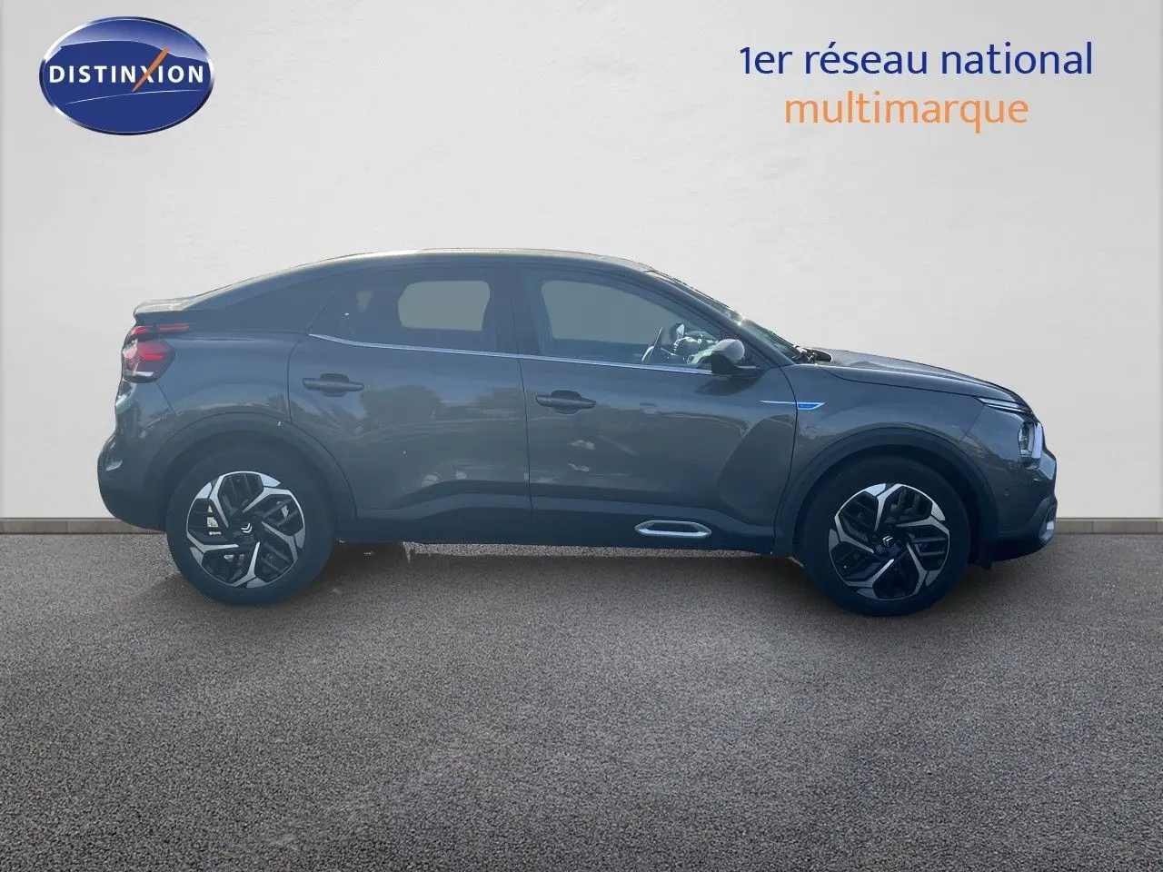 Profil droit d'une Citroën C4 2023 gris métallisé avec jantes noires et détails chromés sous un mur blanc.