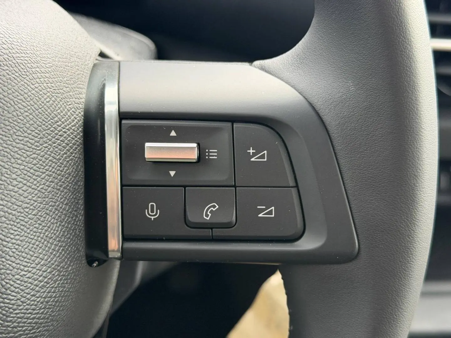 Gros plan sur les commandes audio et téléphone intégrées au volant noir de la Citroën C4 électrique 2024.