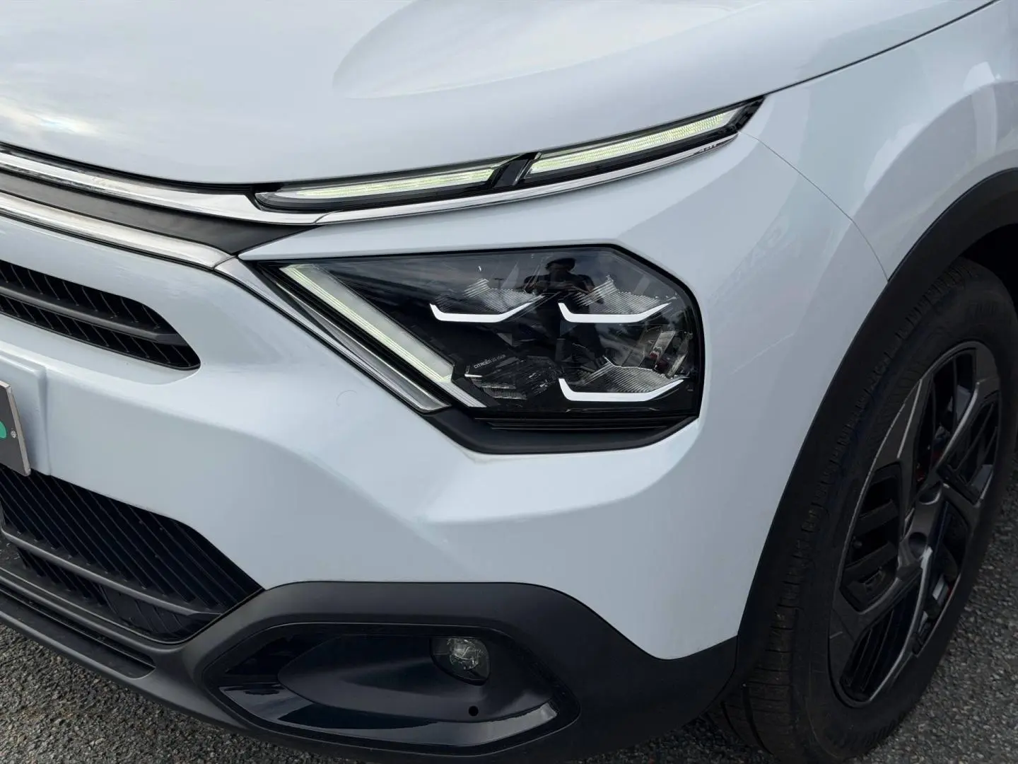 Gros plan sur l’avant droit blanc du Citroën C4 électrique 2024, mettant en valeur les phares LED et la roue noire.