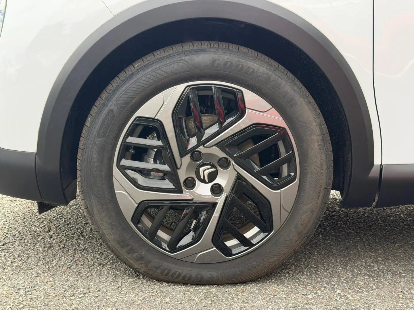 Gros plan sur la roue avant droite blanche d'une Citroën C4 électrique 2024 avec jante au design géométrique noir et argent.