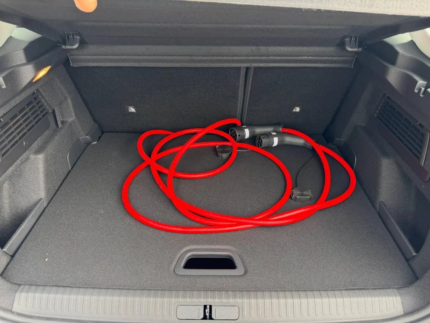 Coffre ouvert d'une Citroën C4 électrique blanche, vue de dessus, avec câble de recharge rouge enroulé.