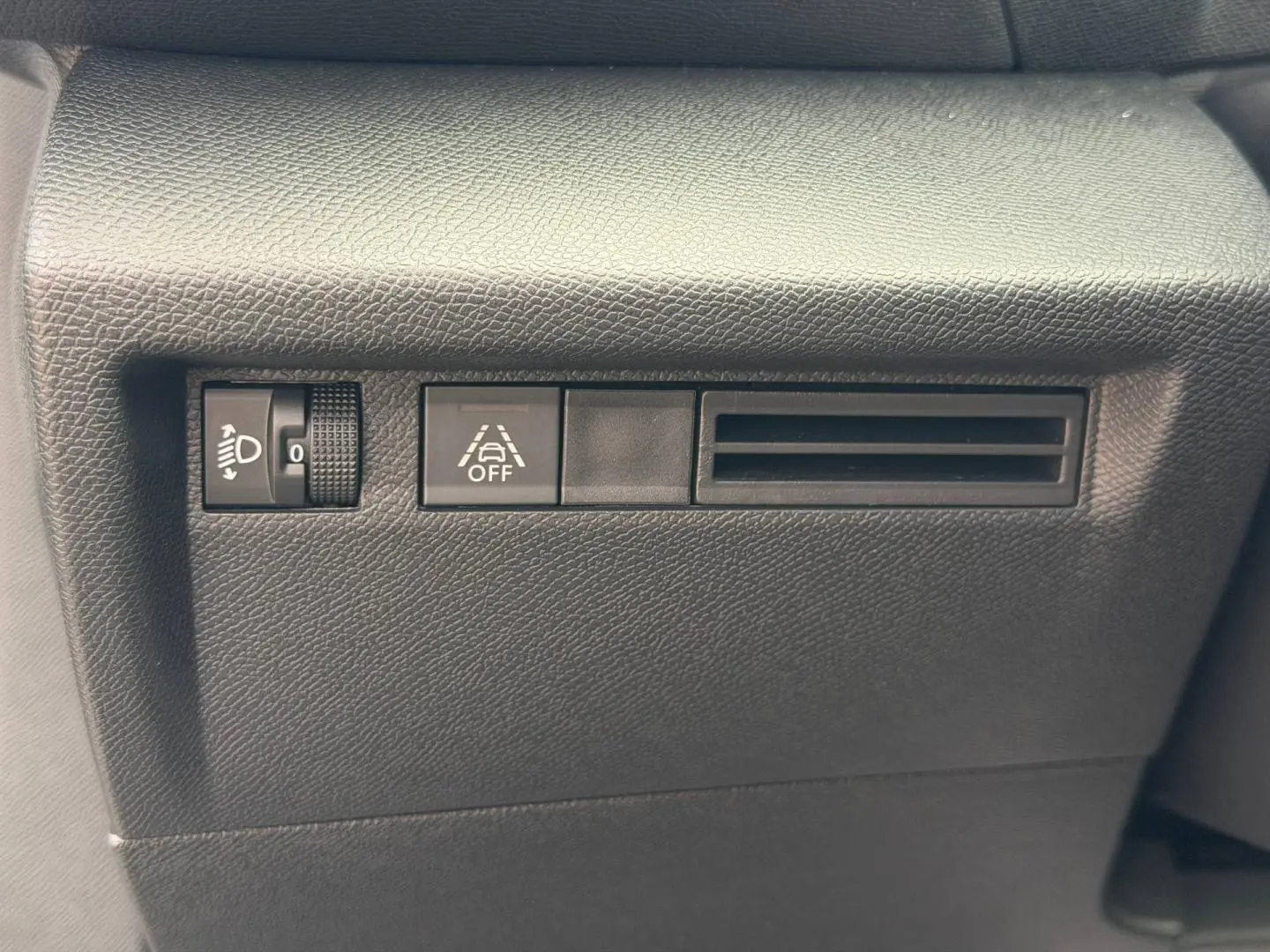 Détail du tableau de bord noir avec commande de réglage des phares, bouton d'alerte et prise d'air sur Citroën C4 électrique.