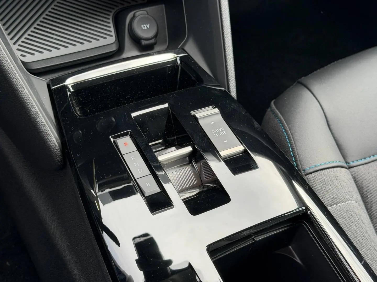 Gros plan sur la console centrale noire brillante avec levier de vitesses automatique et bouton Drive Mode, siège tissu gris visible.