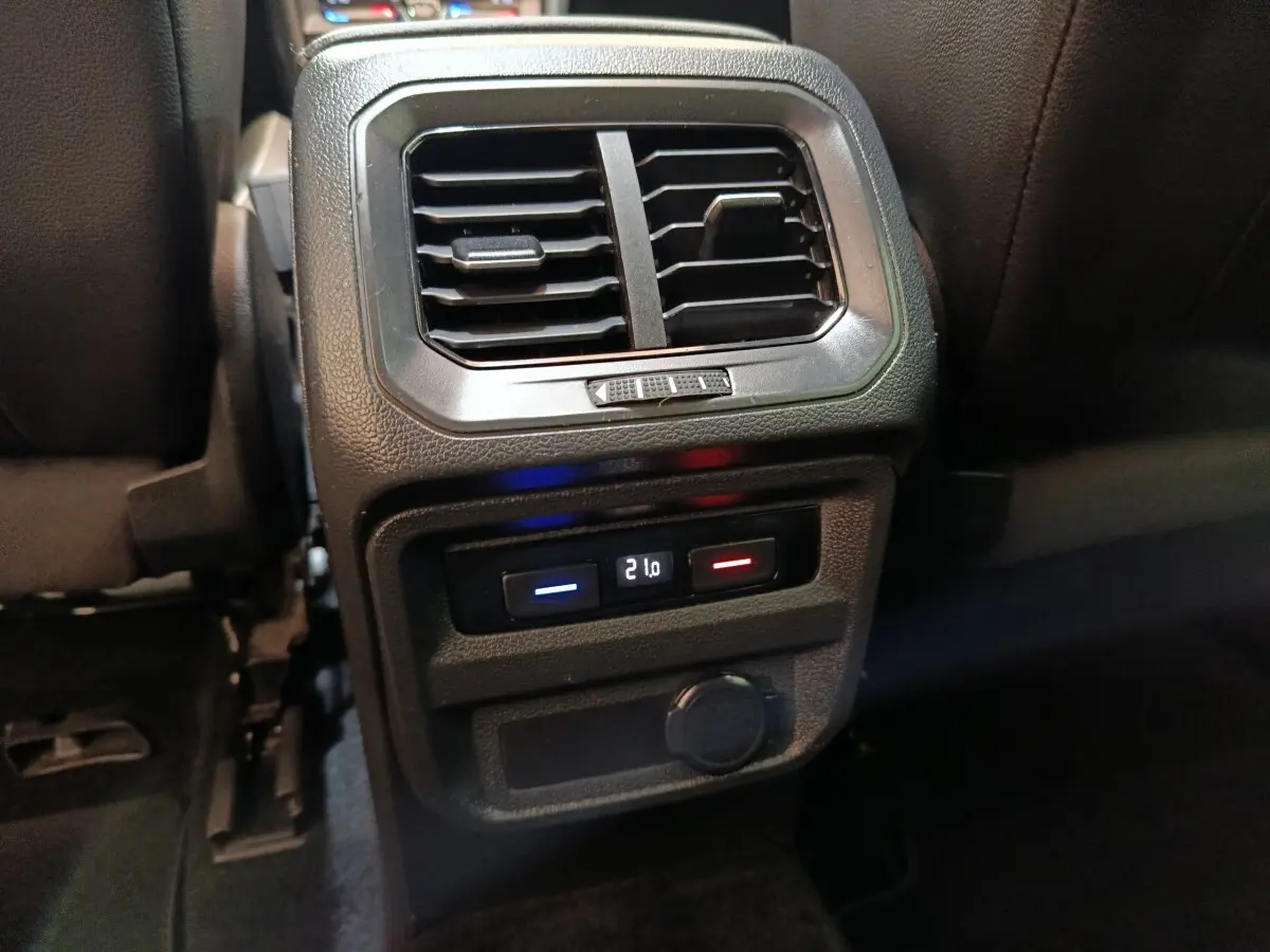 Vue rapprochée de la console centrale arrière noire du Volkswagen Tiguan 2.0 TDI avec commandes de climatisation et prise 12V.