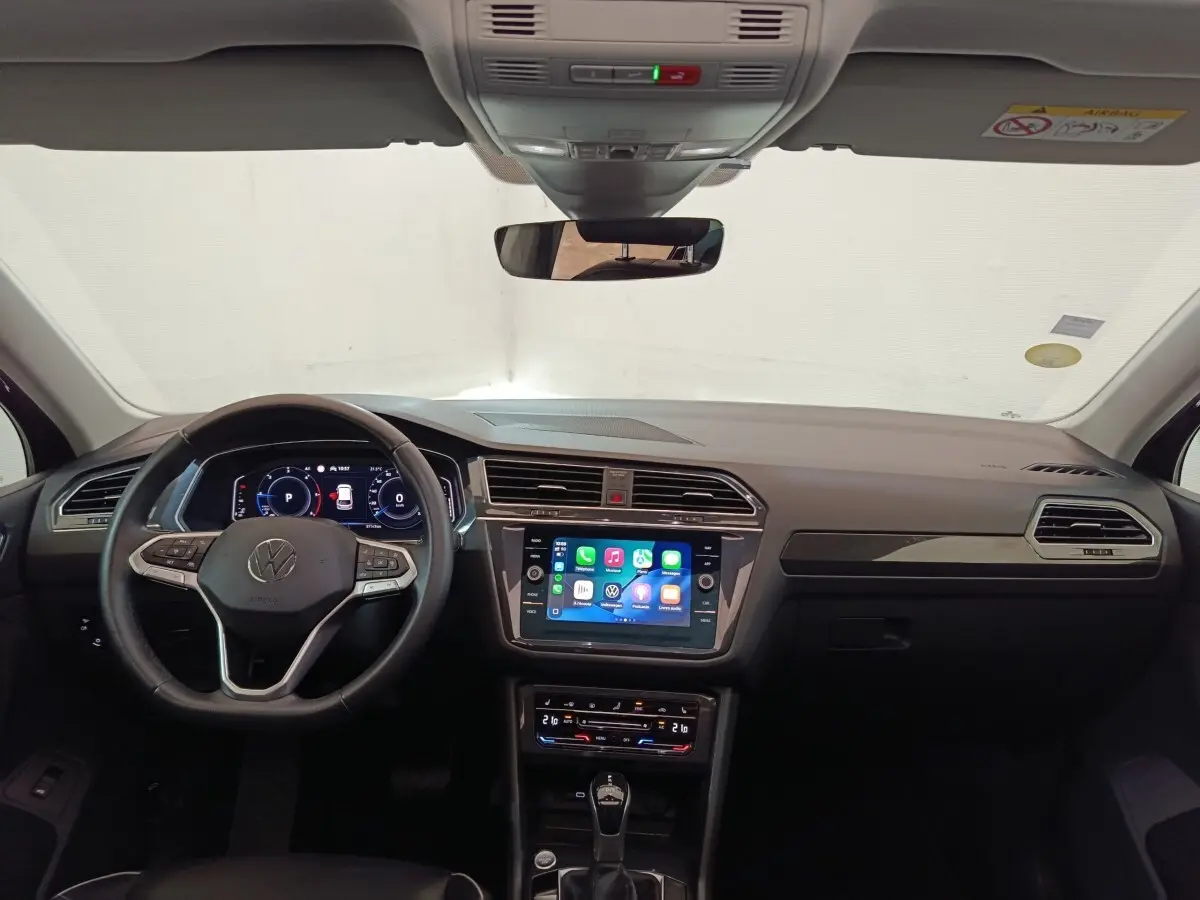 Vue intérieure frontale du Volkswagen Tiguan noir 2021, volant cuir multifonctions et écran tactile central allumé.