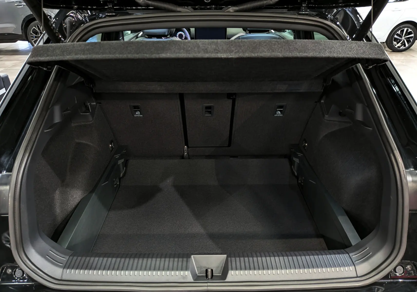 Coffre ouvert vu de l'arrière d'un Volkswagen T-Roc eTSI 150 CH DSG7 R-Line noir Ébène, intérieur spacieux et habillage sombre.