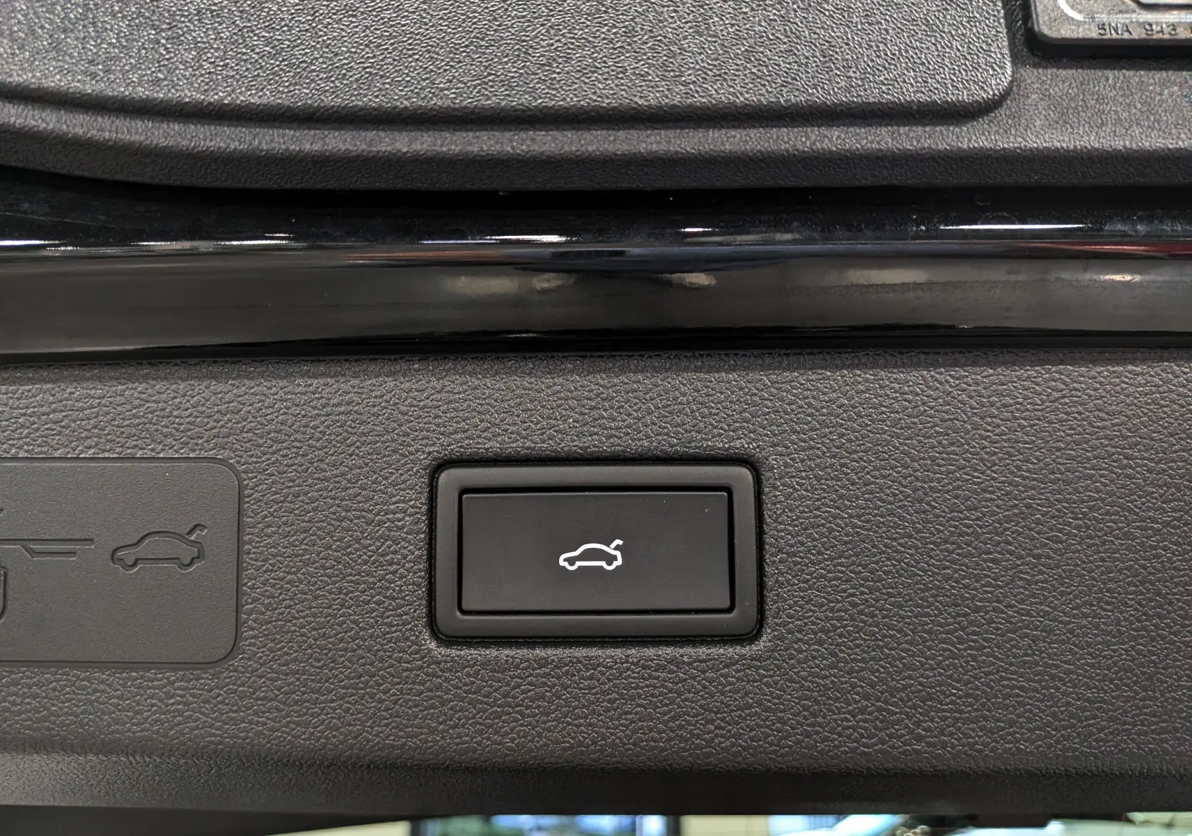 Bouton noir de commande d'ouverture électrique du coffre sur un Volkswagen T-Roc eTSI 150 CH DSG7 R-Line noir Ébène, vue intérieure.
