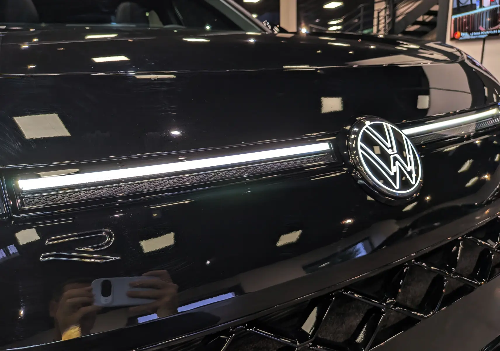 Gros plan sur la calandre noire ébène du Volkswagen T-Roc eTSI 150 R-Line avec logo VW lumineux et bande LED.