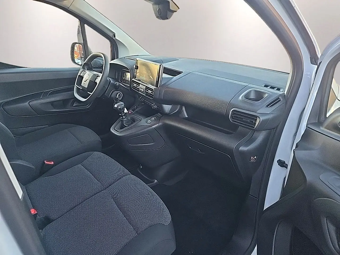 Intérieur avant du Citroën Berlingo Fourgon blanc 2026, vue côté conducteur avec tableau de bord et sièges noirs.