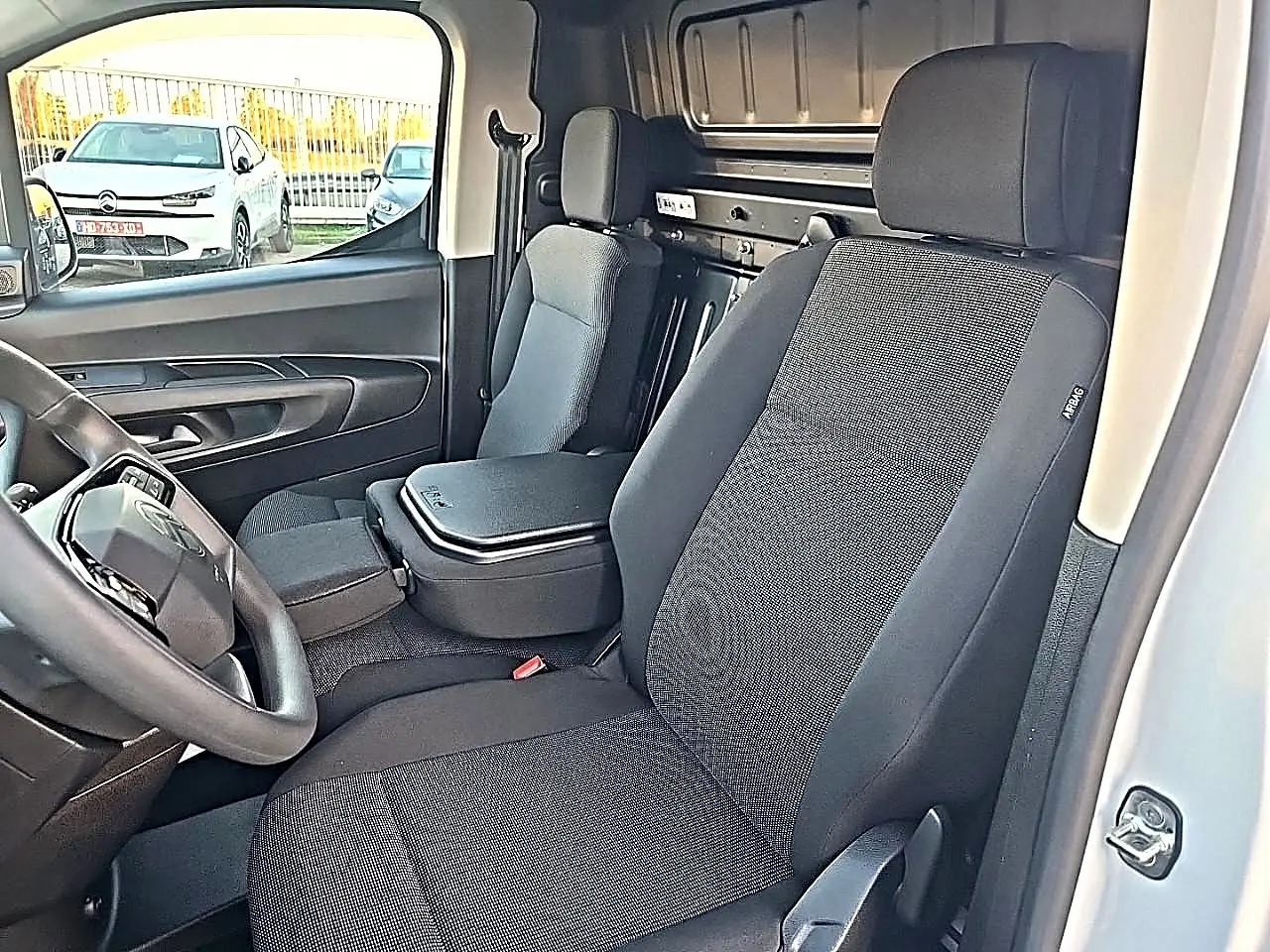 Vue intérieure côté conducteur du Citroën Berlingo Fourgon blanc, montrant les sièges et le volant multifonction.