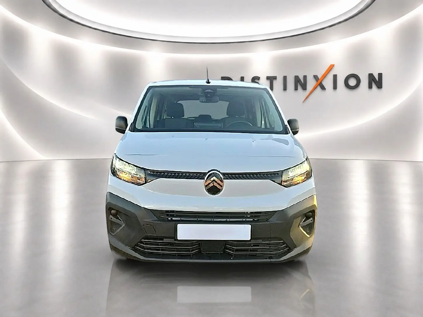 Vue de face d'un Citroën Berlingo Fourgon XL blanc avec phares allumés dans un showroom lumineux.