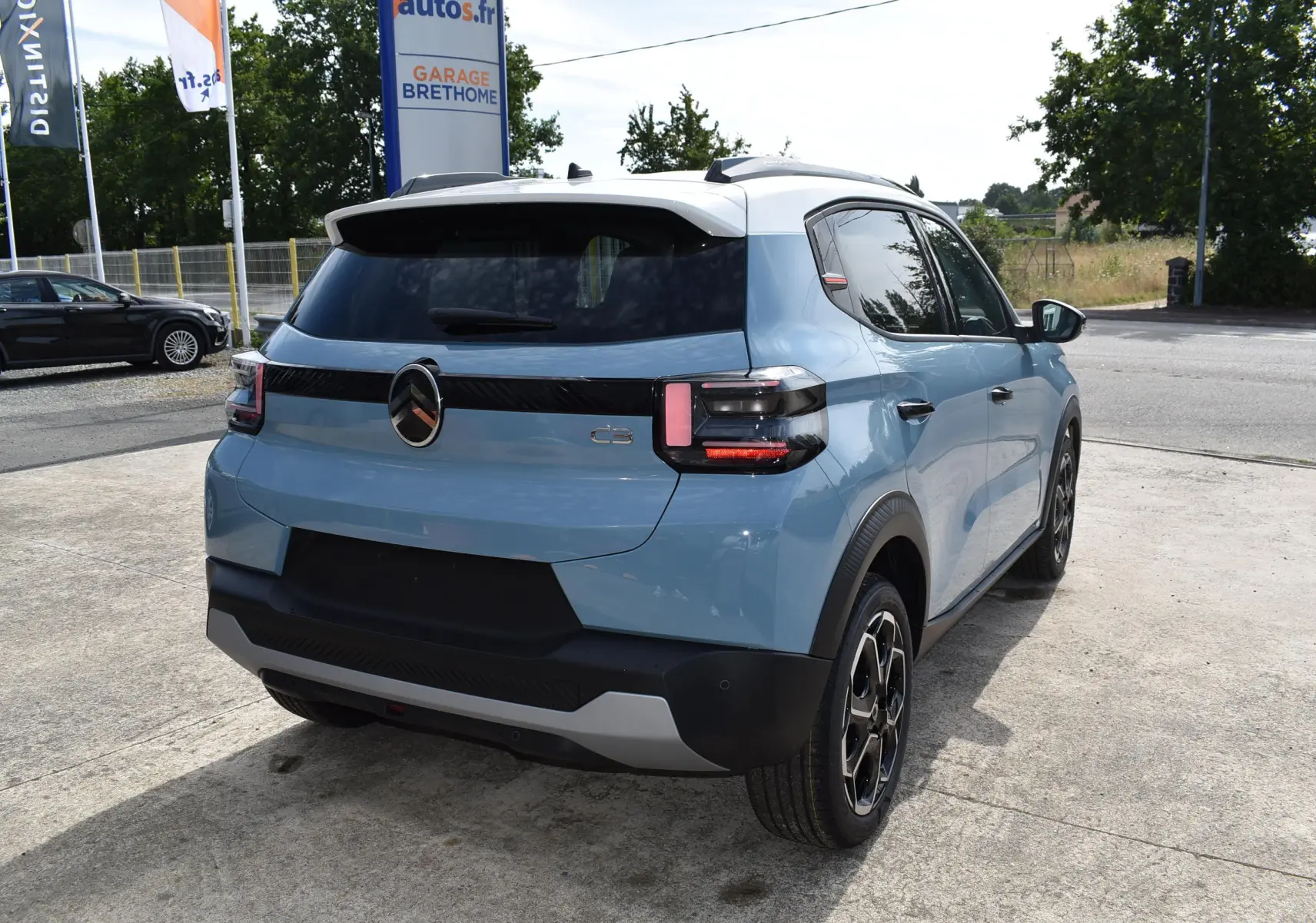 Vue 3/4 arrière droite d'une Citroën C3 2025 bleu avec toit noir et jantes biton sur parking extérieur.